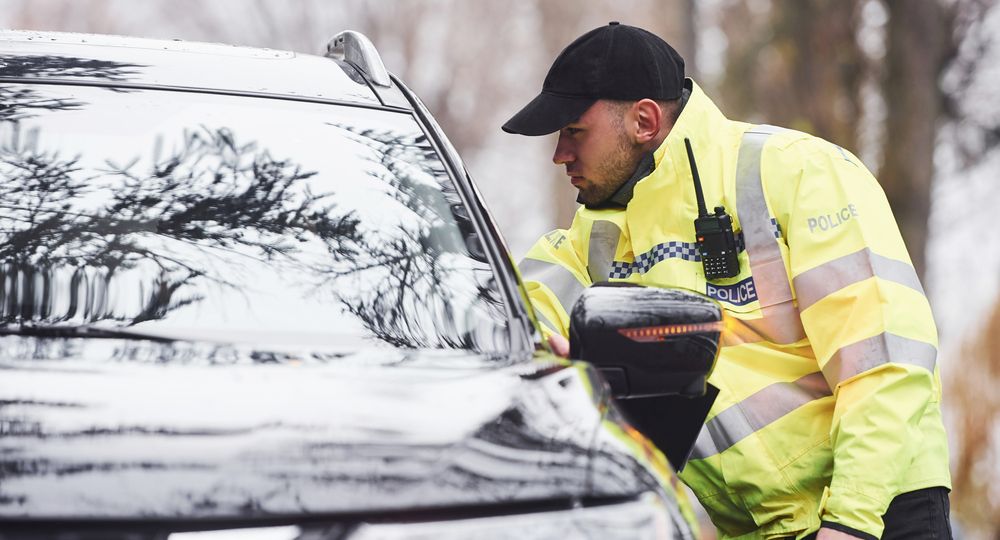 Male police officer in green uniform checking vehicle on the road