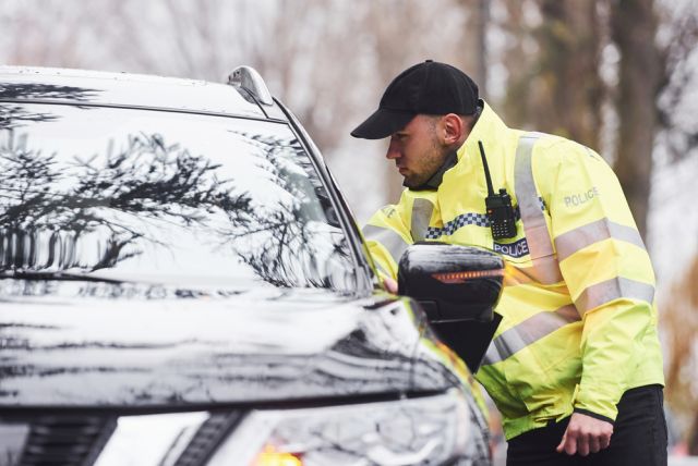 Male police officer in green uniform checking vehicle on the road