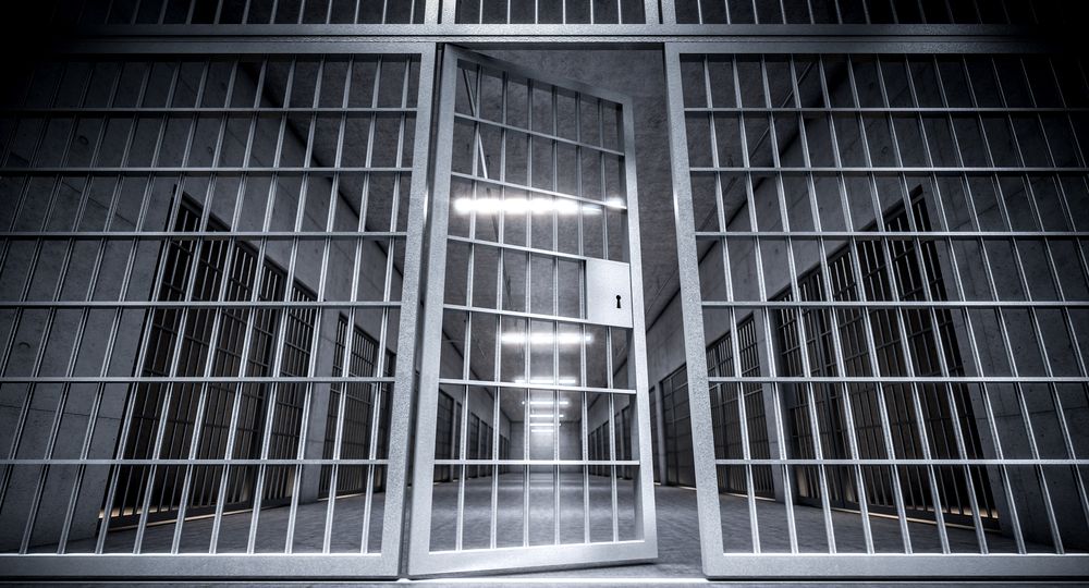 corridor of a prison with bars and open cell door.