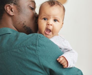 Back view portrait of young African-American father holding son with cute baby looking at camera over mans shoulder, copy space