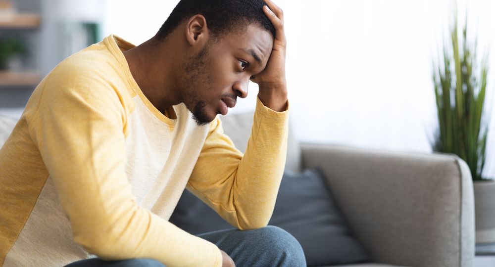 Thoughtful african american man touching his head, home interior