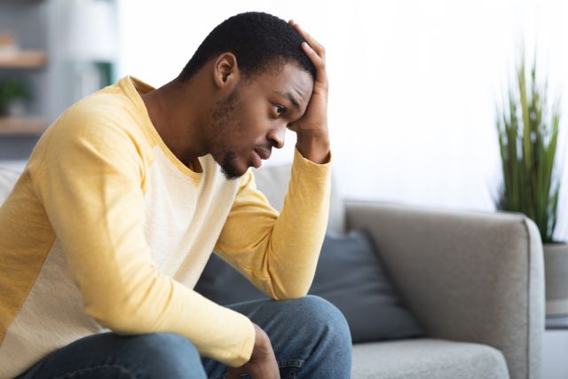 Thoughtful african american man touching his head, home interior