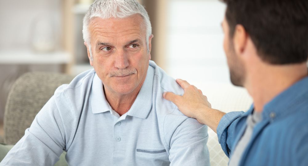 adult son sitting on sofa and talking to father